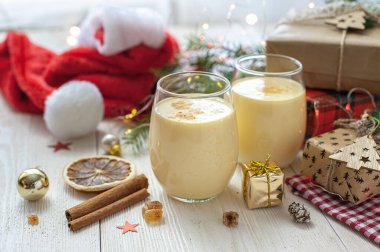 Noel hediyelerinin yanındaki beyaz tahta masada iki bardak eggnog. Tatlı yumurta tatlısı. Noel kahvaltısı. Seçici odak