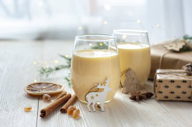 Noel hediyelerinin yanındaki beyaz tahta masada iki bardak eggnog. Tatlı yumurta tatlısı. Noel kahvaltısı.