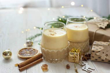 Noel hediyelerinin yanındaki beyaz tahta masada iki bardak eggnog. Tatlı yumurta tatlısı. Noel kahvaltısı. Seçici odak