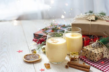 Noel hediyelerinin yanındaki beyaz tahta masada iki bardak eggnog. Tatlı yumurta tatlısı. Noel kahvaltısı.