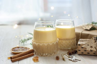 Noel hediyelerinin yanındaki beyaz tahta masada iki bardak eggnog. Tatlı yumurta tatlısı. Noel kahvaltısı.