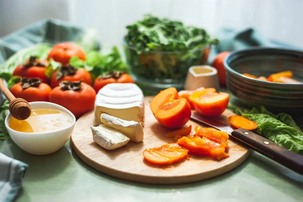 Состав и процесс приготовления витаминного зимнего салата с хурмой, мандаринами и сыром. Селективный фокус Веганский салат приготовления. Здоровое питание. — стоковое фото