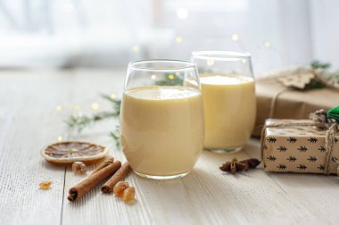 Noel hediyelerinin yanındaki beyaz tahta masada iki bardak eggnog. Tatlı yumurta tatlısı. Noel kahvaltısı. Seçici odak