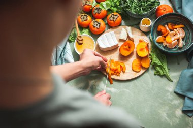 İçindekiler ve vitamin kış salatası hazırlama süreci hurma, mandalina ve peynirle kadın veya genç el kesimi hurma ağaçları üzerinde yuvarlak ahşap bir tahta üzerinde vegan öğle yemeği hazırlığı.