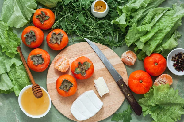 Ingrédients et processus de fabrication d'une salade d'hiver vitaminée aux kaki, mandarines et fromage bleu. Pas à pas. Vue d'en haut. — Photo