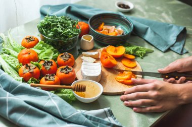 İçindekiler ve hurma, mandalina ve peynirli vitamin kış salatası yapma süreci kadın veya ergen el kesimi hurmaları yuvarlak ahşap bir vegan öğle yemeği hazırlama. Seçici odak