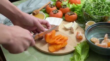 Hurma, mandalina ve maruldan diyet vegan salatası pişirmek. Kamera hareketi. İnsan eli, sağlıklı bir kahvaltı ya da öğle yemeği için meyve keser..