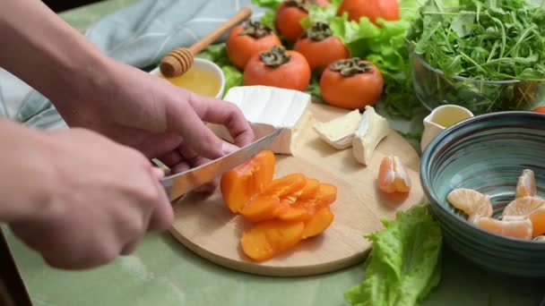 Cocción de ensalada vegana dietética a partir de caquis, mandarinas y lechuga. movimiento de la cámara. Las manos humanas rebanan fruta para un desayuno o almuerzo saludable. — Vídeos de Stock