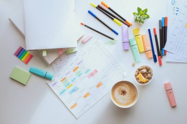 Top view of the white work desk with colourful stationery. Students schedule for the week. Planning a working week with coffee and snacks. layout.