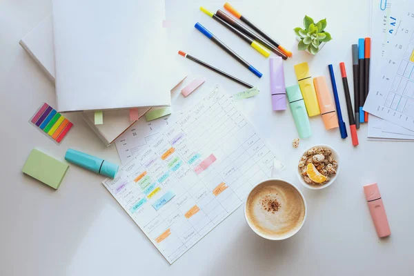 Top view of the white work desk with colourful stationery. Students schedule for the week. Planning a working week with coffee and snacks. layout. Zdjęcia Stockowe bez tantiem