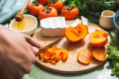 İçindekiler ve hurma, mandalina ve peynirli vitamin kış salatası yapma süreci kadın veya ergen el kesimi hurmaları yuvarlak ahşap bir vegan öğle yemeği hazırlama. Seçici odak