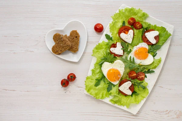 Reggeli Valentin napon. Egy tál szív alakú rántotta, paradicsom, sajt, gyógynövények és gabonakenyér. Kilátás fentről. Helyet a szövegnek. Diétás reggeli. — Stock Fotó