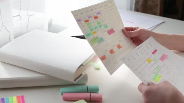 Programación y planificación de la semana. Gestión del tiempo del estudiante. Las manos de las mujeres escriben el horario en un pedazo de papel y marcan con un marcador en una mesa blanca en un día soleado. Vista lateral. — Vídeos de Stock