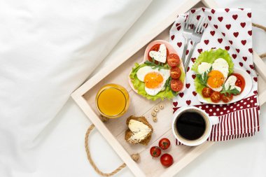 Sevgililer Günü 'nde yatakta tepside kahvaltı. İçinde yumurta, domates, peynir, kahve ve meyve suyu olan iki kalp şeklinde tepsi. İki kişi için bir otel odasında kahvaltı. Yukarıdan görüntüle.