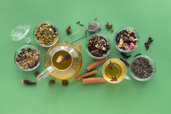 Kilka odmian herbaty ziołowej i owocowej w szklanych miskach i czajnik z filiżanką gorącej herbaty na zielonym tle. Widok z góry. Zdrowe odżywianie. Pyszny napój rozgrzewający. Zdjęcie Stockowe