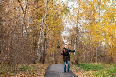 Genç bir çocuk sonbahar parkında yürür ve bir video çeker. Siyah ceketli beyaz bir çocuk akıllı telefonlu bir monopod tutuyor. Blogcu. Duygusal iletişim..