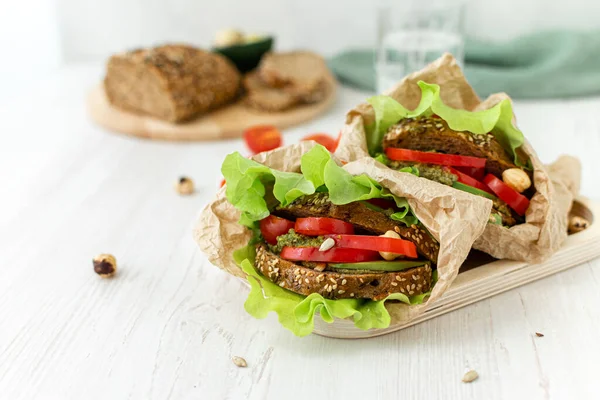 Vegan sandwiches of whole grain bread, tomatoes, peppers and avocados with spicy sauce and lettuce leaves wrapped in paper on a wooden tray. Close-up. Healthy food. Diet breakfast. — Stock Photo, Image