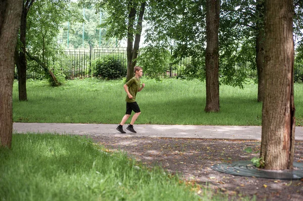 Een tienerjongen doet aan sport. Lopende training. Ochtend joggen door het zomerpark. Een gezonde levensstijl. Hobby 's van tieners. — Stockfoto