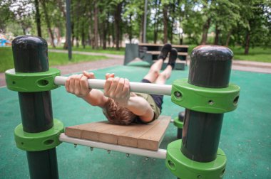 Genç çocuk parktaki simülatörlerle spor yapıyor. Gençlerin sağlıklı aktiviteleri. Ağırlık bankında karın kası yapan bir çocuk. Sağlıklı bir yaşam tarzı. Gençlerin hobileri. Yüksek kalite fotoğraf