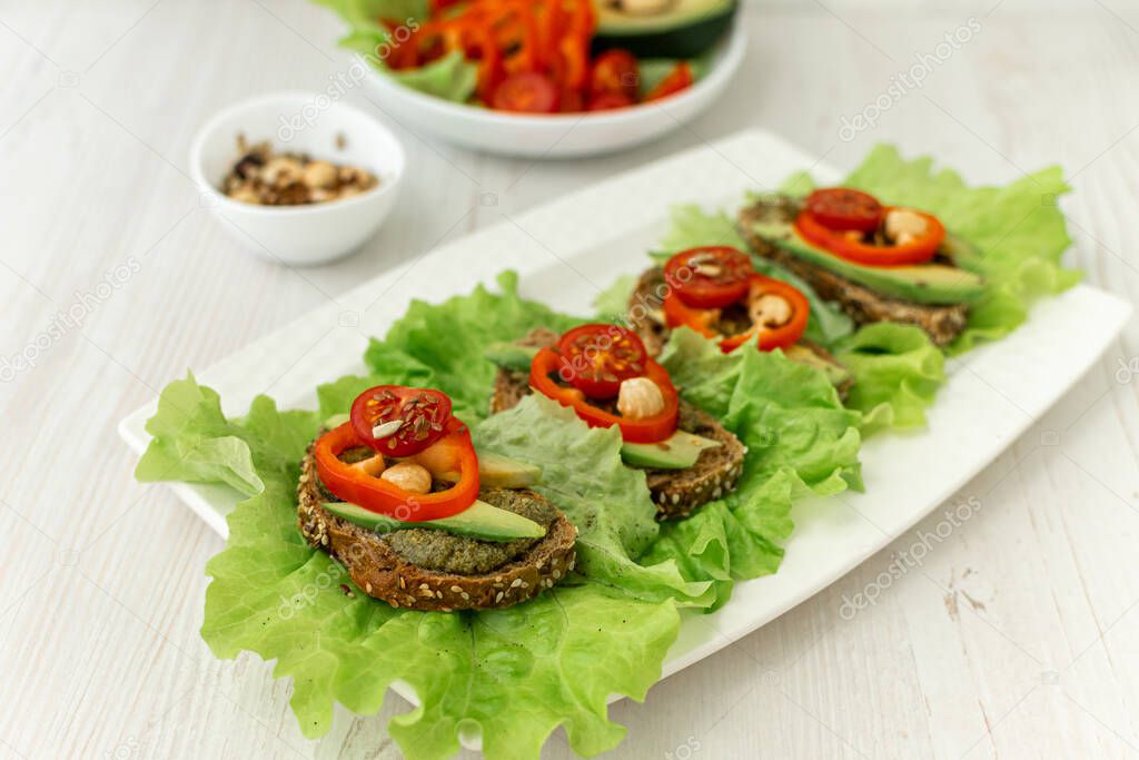 Sandwiches with rye bread, tomatoes, avocados, peppers and spicy sauce on a white plate covered with lettuce. Diet breakfast. healthy eating. Vegan snack Side view, close-up