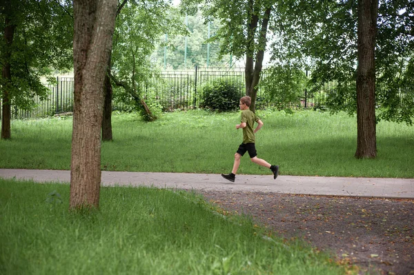 Tieners ochtend. Gezonde levensstijl en sport. Een tienerjongen loopt langs het pad van een zomerpark. Lopende training. Gezondheidszorg. — Stockfoto