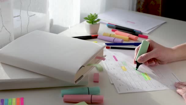 Programación y planificación de la semana. Gestión del tiempo del estudiante. Las manos de las mujeres escriben el horario en un pedazo de papel y marcan con un marcador en una mesa blanca en un día soleado. Vista lateral. — Vídeo de stock