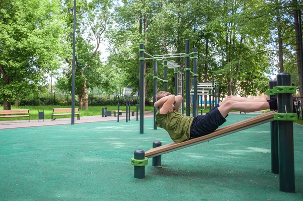 Genç çocuk parktaki simülatörlerle spor yapıyor. Gençlerin sağlıklı aktiviteleri. Ağırlık bankında karın kası yapan bir çocuk. Sağlıklı bir yaşam tarzı. Gençlerin hobileri. Vücut bakımı ve sağlık.