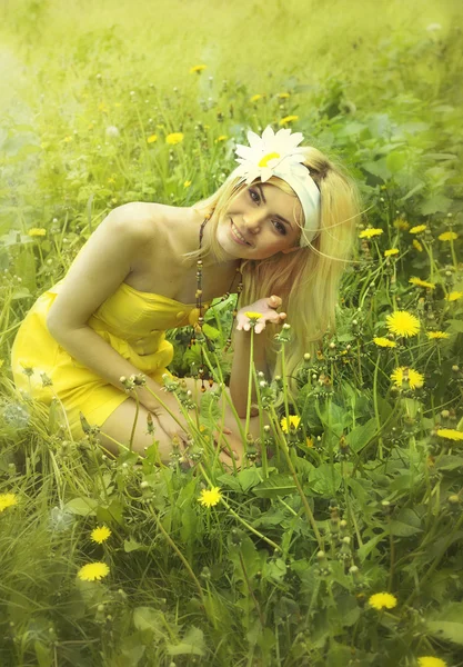 Mooie vrouw in gele jurk zittend op een gras. — Stockfoto