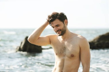 Okyanus kenarında gülümseyen genç adam portresi, üstsüz vücut.