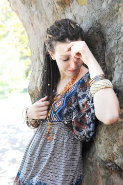 Güneşli bir açık hava parkında poz veren rastalı saç stiliyle neşeli genç kadın portresi.