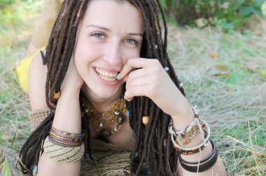 Rasta saç stiliyle gülümseyen genç kadın portresi güneşli bir parkta poz veriyor, kameraya bakıyor, kadın çimlerin üzerinde dinleniyor.