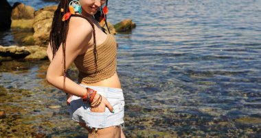 Güneşli deniz manzarasına karşı kadın, kot şortlu kadın, rastalı kadın yaz tatilinin tadını çıkar.