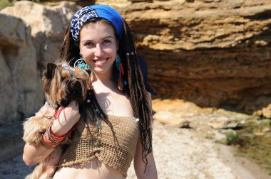 Mutlu gülümseyen genç kadın ve Yorkshire teriyer köpeği, sarı bir kayanın üzerinde poz veriyorlar.