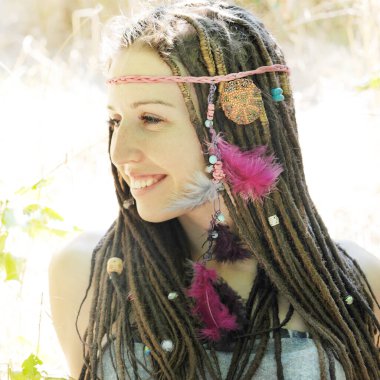 Mutlu gülümseyen şirin kadın portresi Rastalı saç stili süslü boncuklar ve tüyler Parkta güneşli bir günün tadını çıkar