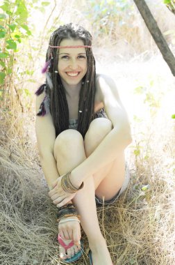 Mutlu, gülümseyen bir kadın oturur, bacaklarına sarılır ve parkta dinlenir, kameraya bakar, açık havada güneşlenir.