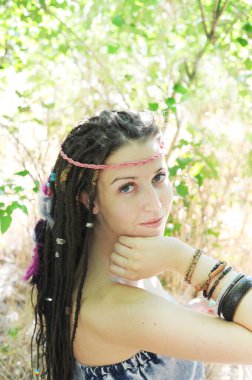 Rasta desenli, çeşitli boncuklu, renkli tüylü, açık hava güneşli genç kadın portresi.