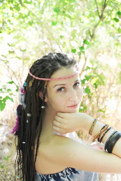 Rasta desenli, çeşitli boncuklu, renkli tüylü, açık hava güneşli genç kadın portresi.