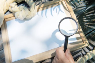 Boş ahşap çerçeve, ip ve büyüteçle bir el, açık hava yaz fotoğrafı, deniz tarzı, palmiye gölgesi