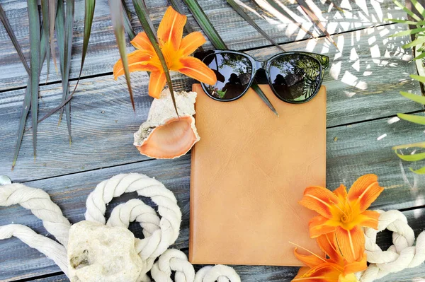 Empty brown book mock up with lily flowers and sunglasses on a wooden table