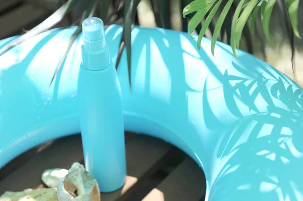 Turquoise sunscreen cream bottle empty mockup with swim ring and palm leaves