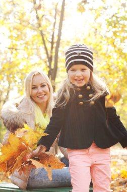 Happy family portrait, blonde mother and daughter in autumn forest, girl with leaves bouquet