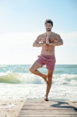 Genç adam okyanus kenarında yoga yapıyor.