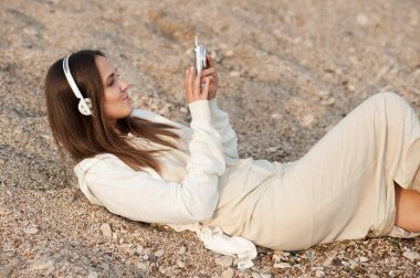 Deniz kumu üzerinde uzanmış gülümseyen ve eski tarz telefonda müzik dinleyen tatlı bir kadın.