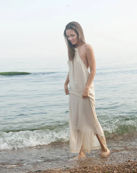 快乐的年轻女子在海滨徒步旅行 身穿白色长裙的女子在水里散步 — 图库照片