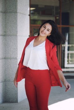 Güzel esmer, açık havada çekilmiş genç bir kadın, kırmızı klasik pantolon giymiş mutlu bir iş kadını.