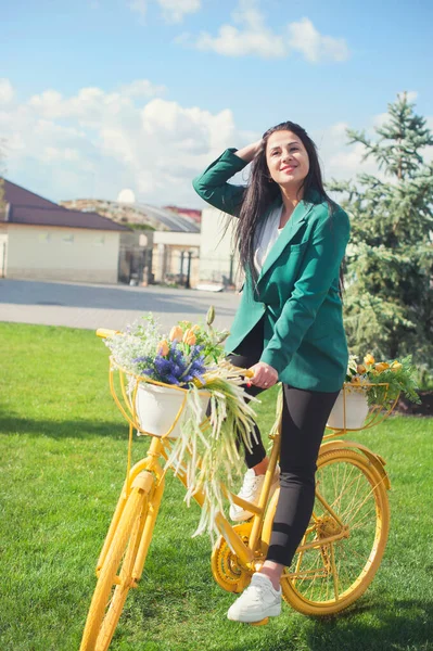 街の周りに花のバスケットと黄色の自転車に乗って美しい若い女性 — ストック写真