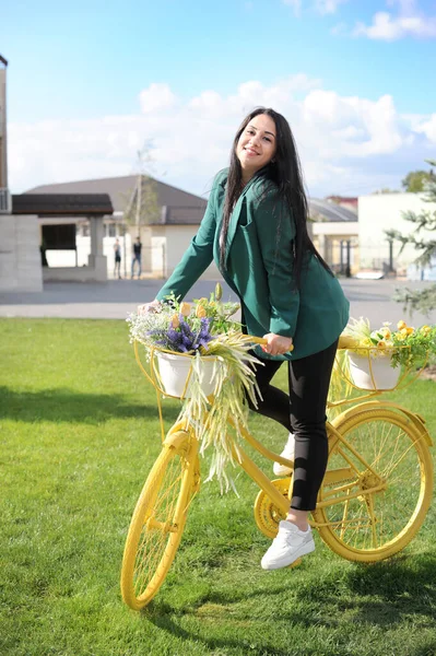 美丽的年轻女子骑着一辆黄色的自行车 满城都是花篮 — 图库照片
