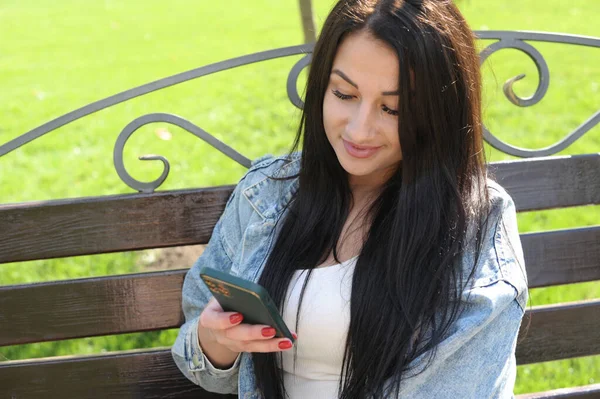 美丽的年轻女子在城市公园休息 在她的社交网络上通过电话观看 — 图库照片