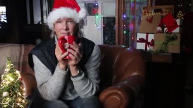Noel Baba şapkalı yalnız Kafkasyalı son sınıf öğrencisi Noel Kar Küresi 'ne bakıyor, elinde Noel ağacı ve hediyelerle. Noel, Covid 19 salgını sırasında şenlik