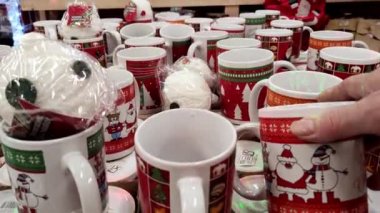 Noel satışları ve alışveriş. Mağazadaki kadınlar Noel çizimleri olan kırmızı-yeşil bardakları parmaklıyor.